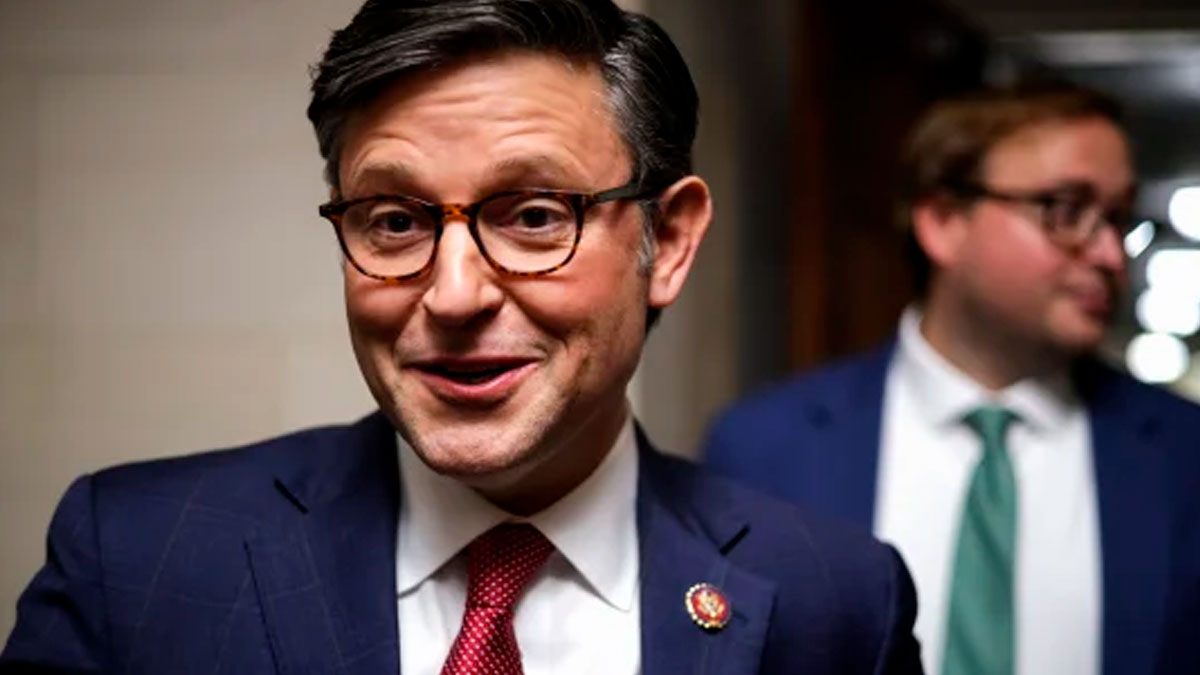 Man in glasses and suit speaking during event, capturing the sad and uninspiring dystopia in a modern setting.