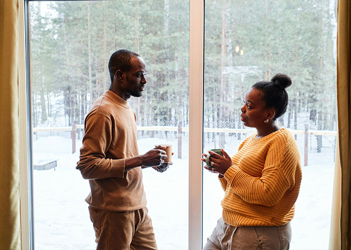 Couple having a serious conversation over coffee near a window with a snowy forest, revealing relationship truths during holiday gift exchange. Couple having a serious conversation over coffee near a window with a snowy forest, revealing relationship truths during holiday gift exchange.