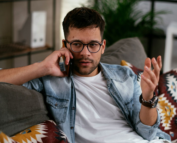 Man in casual clothes talking on phone at home, discussing gym time and babysitting arrangements.
