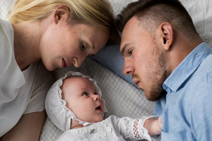 Couple and baby lying down looking at each other, highlighting challenges of balancing gym time and babysitting duties.
