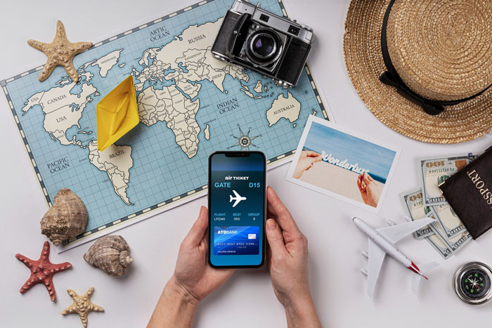 Hands holding phone with digital boarding pass near travel map, camera, hat, and toy airplane symbolizing Hawaii trip plans canceled. Hands holding phone with digital boarding pass near travel map, camera, hat, and toy airplane symbolizing Hawaii trip plans canceled.