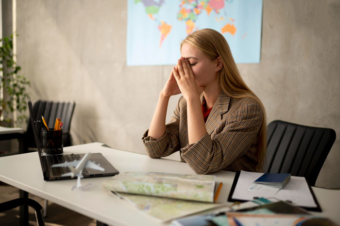 Young woman stressed at desk with travel map and laptop, reflecting tension from canceled Hawaii trip conflict Young woman stressed at desk with travel map and laptop, reflecting tension from canceled Hawaii trip conflict