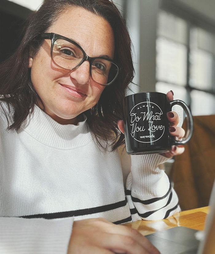 Woman with glasses holding a mug, illustrating emotions related to body-shaming on flight seatmate caught in text.