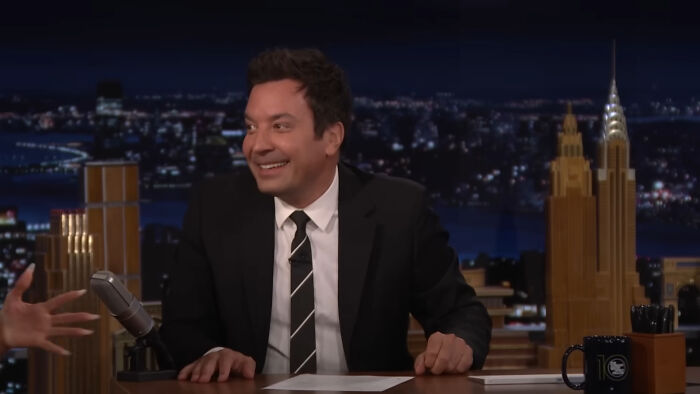 A man in a black suit and striped tie smiling during a late night talk show about people think celebrities closet skeletons.