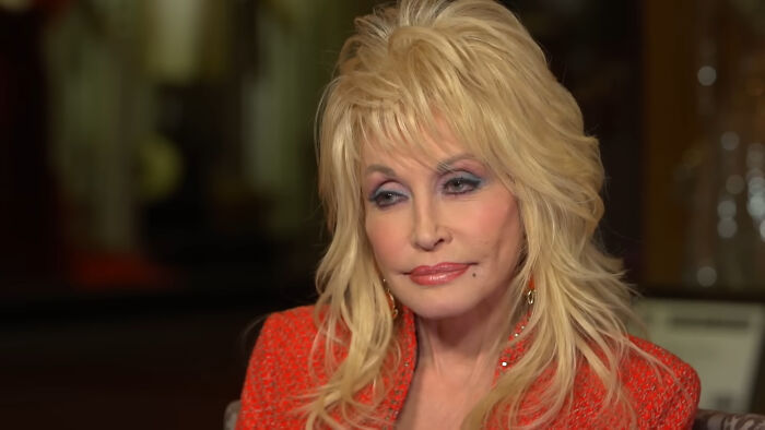 Dolly Parton in a red outfit, sharing fascinating secrets about celebrities in an intimate interview setting.