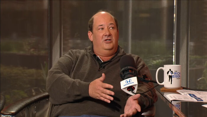 Man in a casual gray sweater sharing fascinating secrets about celebrities during a recorded interview session.