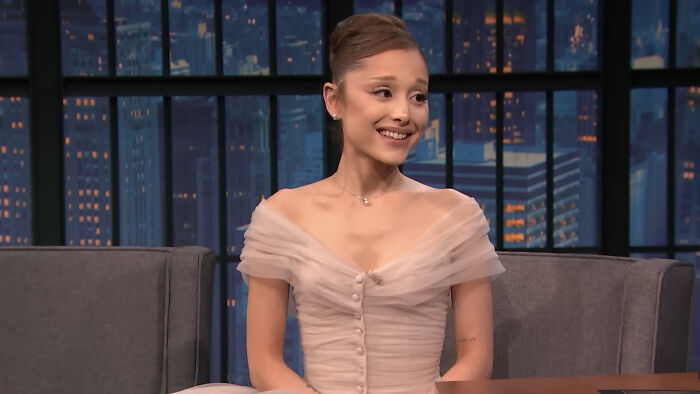 Young woman in an elegant off-shoulder dress smiling during a late-night talk show about celebrities closet skeletons.