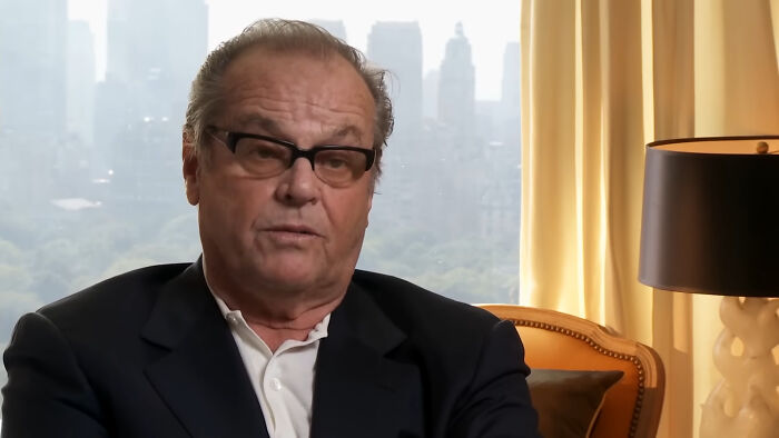 Man wearing glasses and a dark jacket sitting indoors with cityscape background, reflecting on people thinking celebrities have closet skeletons.