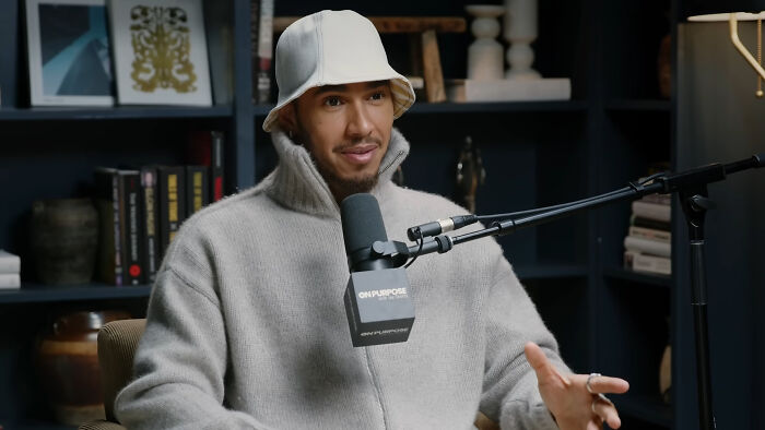 Celebrity wearing a white hat and gray sweater speaking into a microphone during a podcast about celebrities people think suffer.