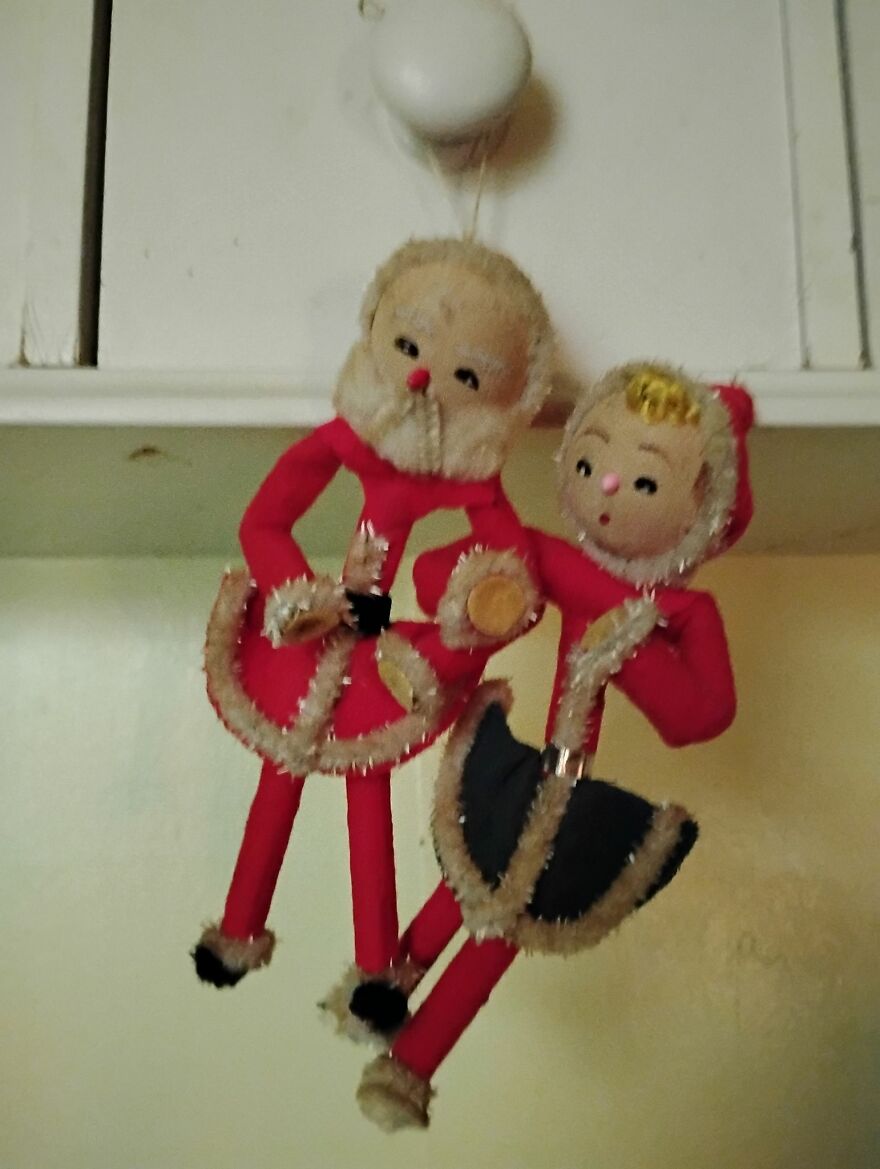 Vintage Christmas decorations featuring two nostalgic Santa and elf dolls in red outfits hanging indoors.