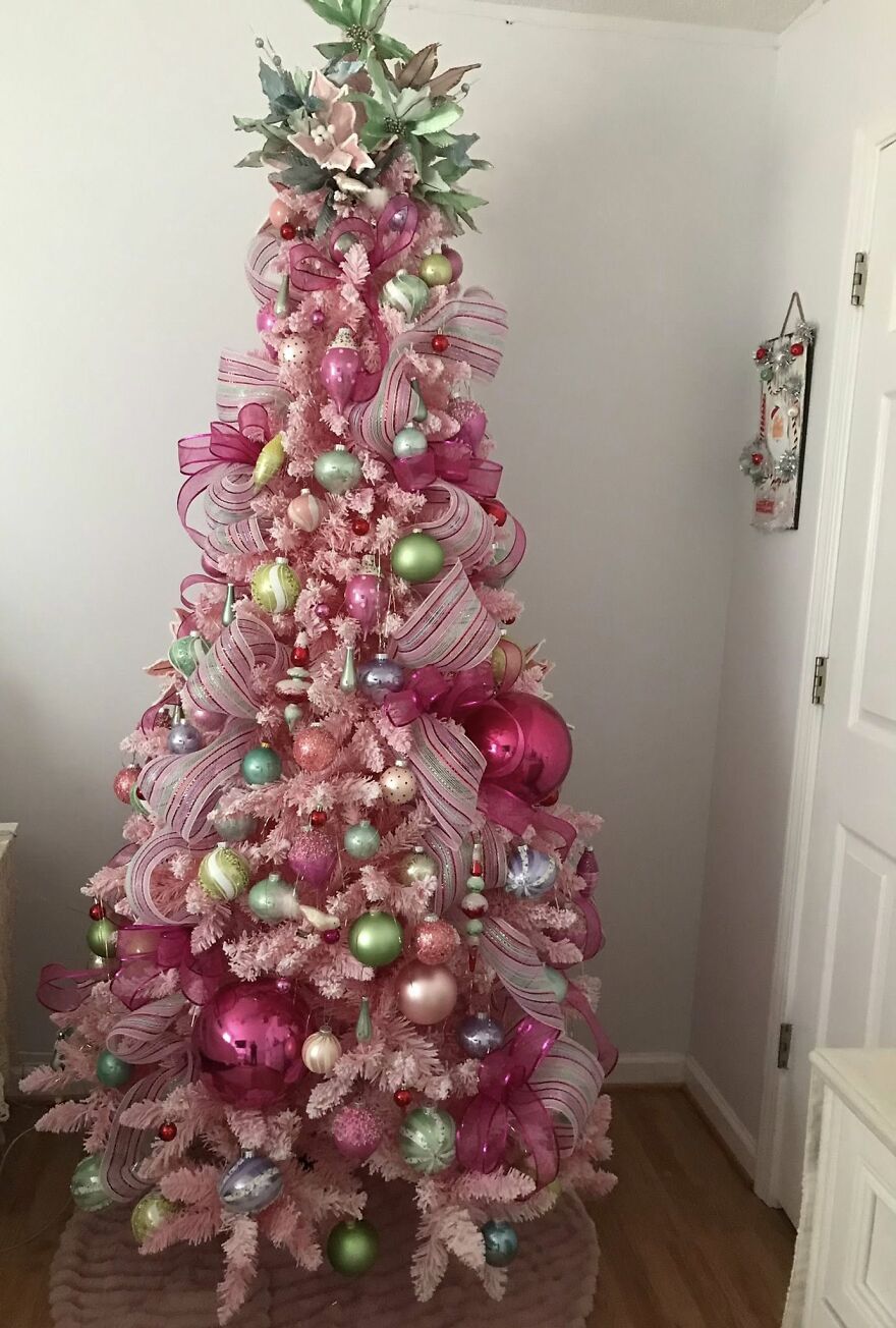 Pink vintage Christmas tree decorated with nostalgic pastel ornaments and striped ribbons in a cozy room setting.
