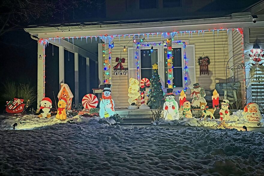 Front porch decorated with nostalgic vintage Christmas decorations including snowmen, candles, and colorful string lights at night.