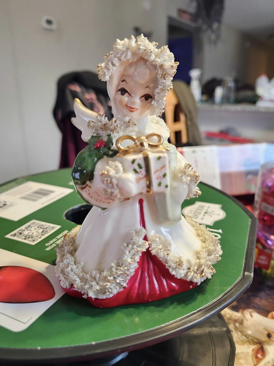 Vintage Christmas decoration figurine of an angel holding a gift, featuring nostalgic holiday details and glitter accents.