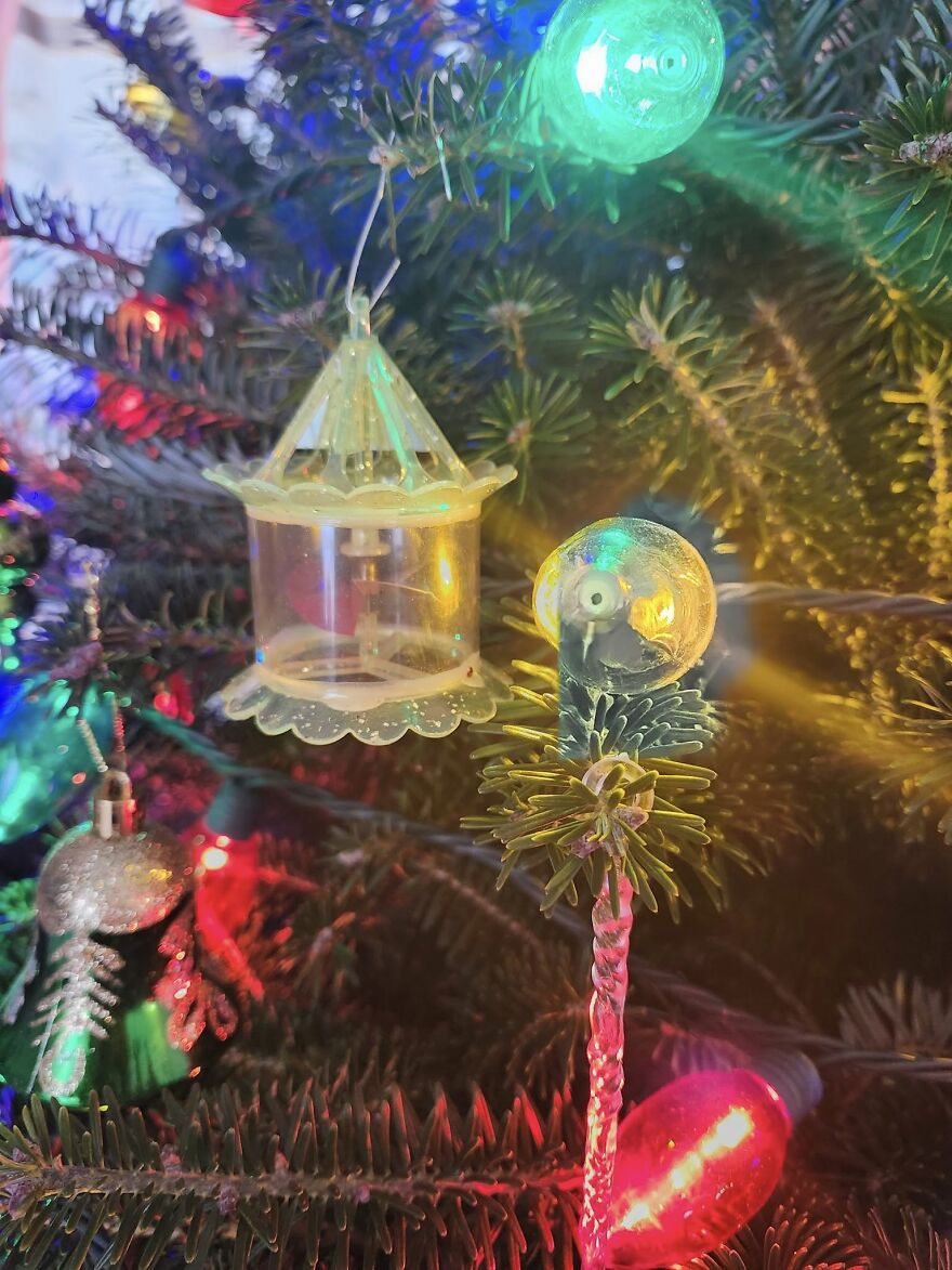 Vintage Christmas decorations hanging on a tree with colorful lights creating a nostalgic holiday atmosphere.