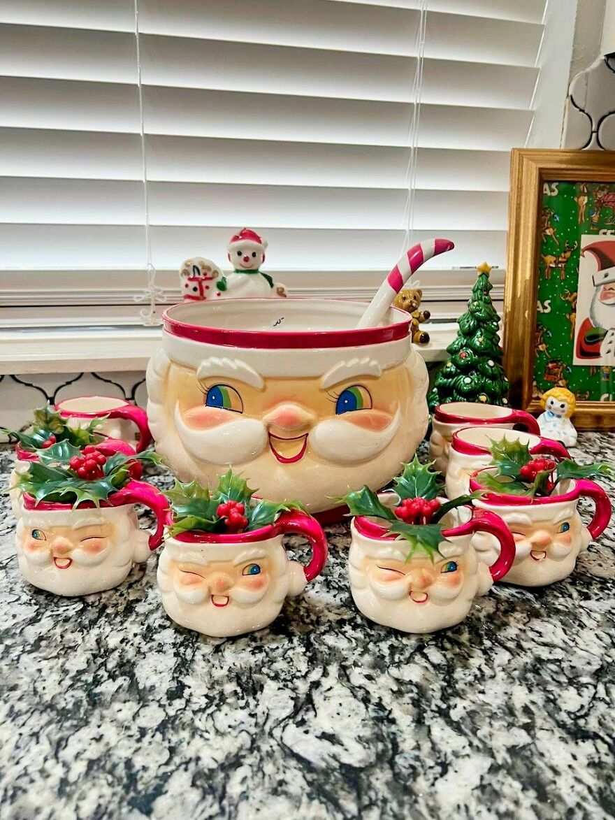 Vintage Christmas decorations featuring Santa-themed mugs and a punch bowl with holly leaves and berries on a granite countertop.