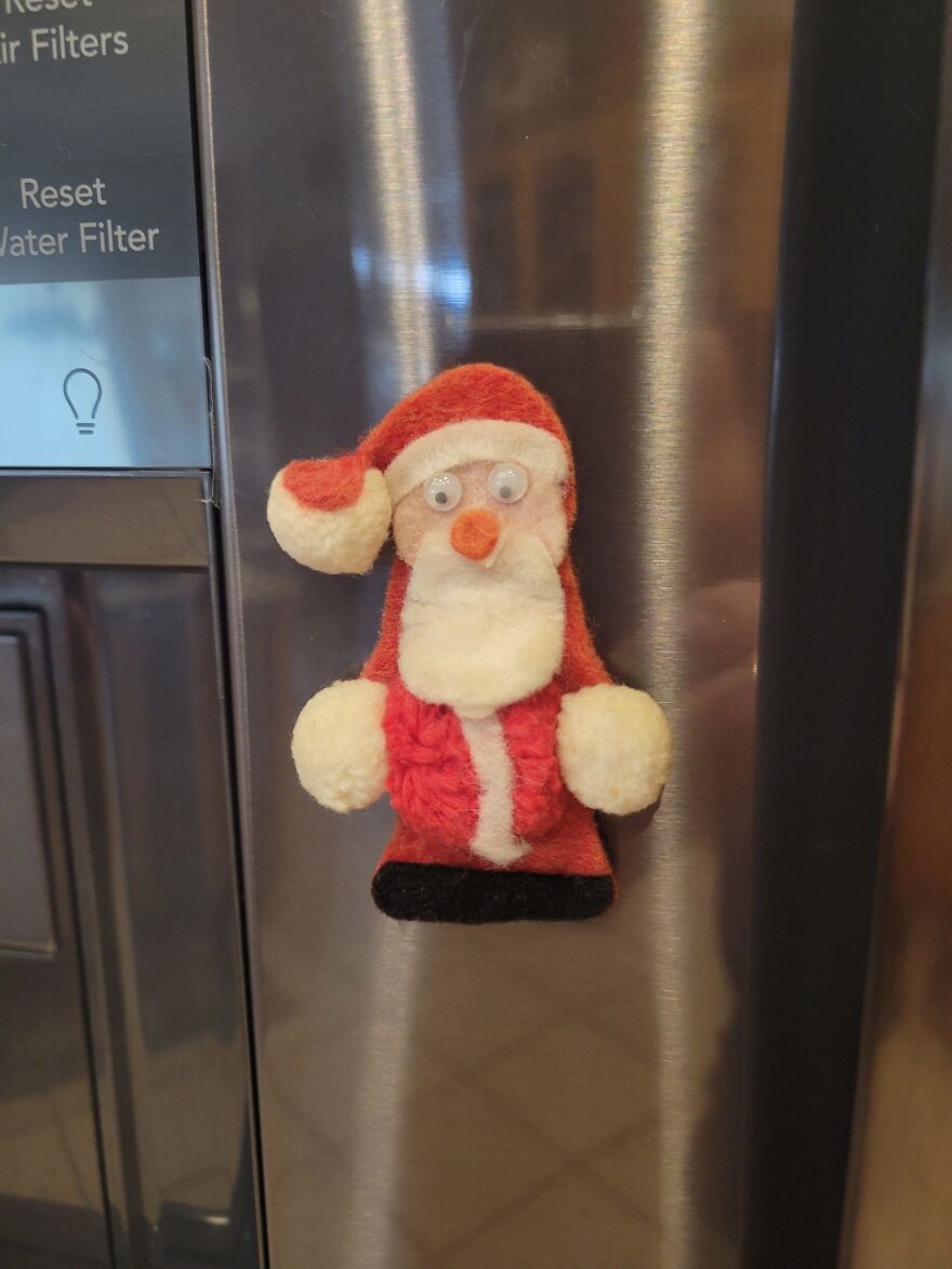 Vintage Christmas decoration of a Santa Claus magnet with felt texture on a stainless steel refrigerator door.
