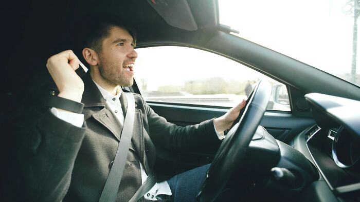 Young man driving a car, celebrating with excitement, illustrating instant karma in everyday life moments.