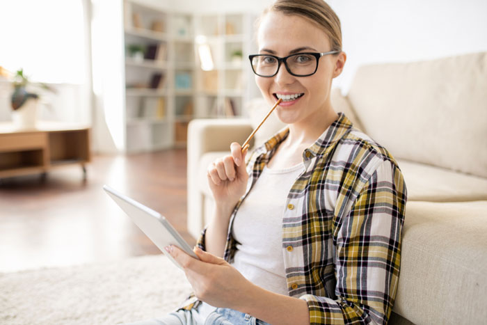 Young woman with glasses sitting on floor using tablet, reflecting on groom ending relationship over debt and wedding costs.