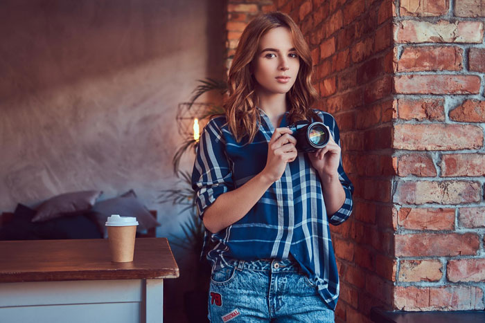 Young woman holding a camera indoors, symbolizing a wedding photographer asked to work for free, showing quiet shock.