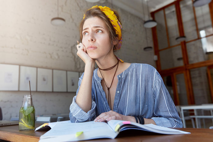 Woman with headband looking shocked and thoughtful while sitting at table with open book, representing wedding photographer request. Woman with headband looking shocked and thoughtful while sitting at table with open book, representing wedding photographer request.