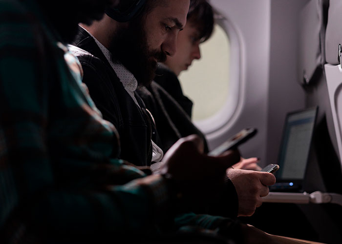 Man focused on his phone inside an airplane cabin, illustrating themes of unintended consequences and personal reflection.