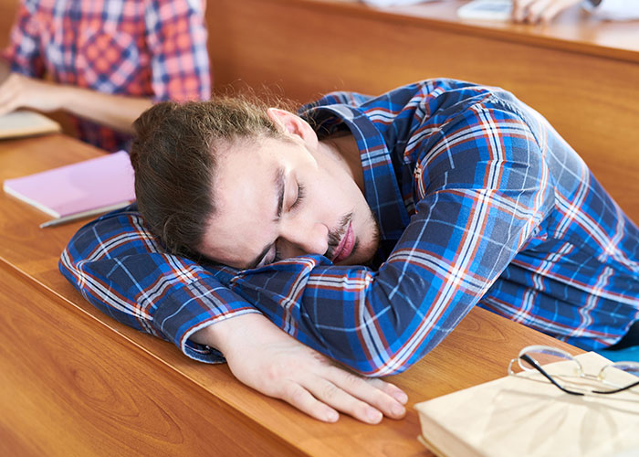 Young man in a plaid shirt sleeping in a classroom, illustrating unintended consequences of drunken jealousy stories