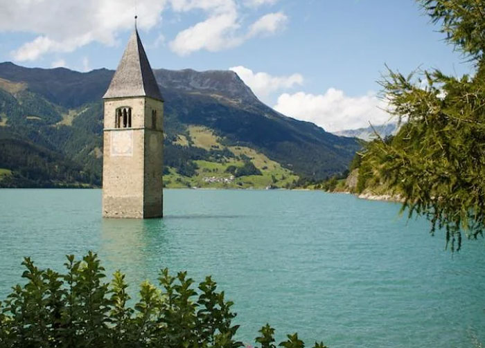 Submerged bell tower in lake surrounded by mountains, unrelated to bread-shaped bread factory or weird buildings.