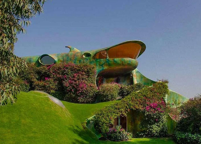 Colorful building covered in greenery with unusual curved shapes, resembling a bread-shaped bread factory in a lush landscape.