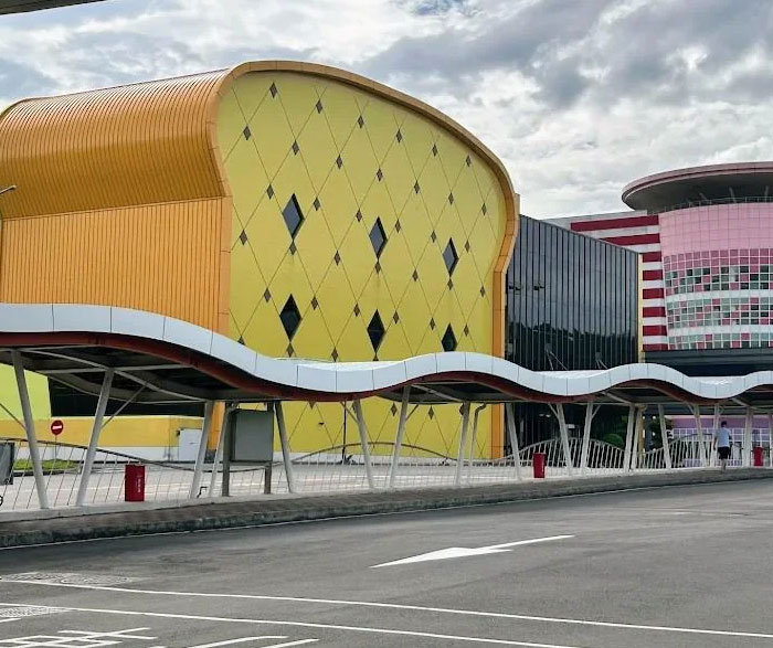 Bread-shaped bread factory building with yellow curved facade and diamond-patterned windows under cloudy sky.