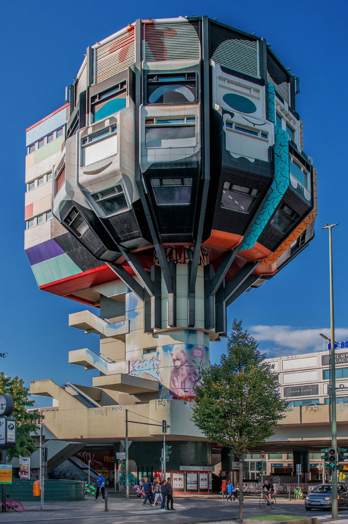 Unusual bread-shaped architecture with colorful panels and graffiti in an urban setting under a clear blue sky.