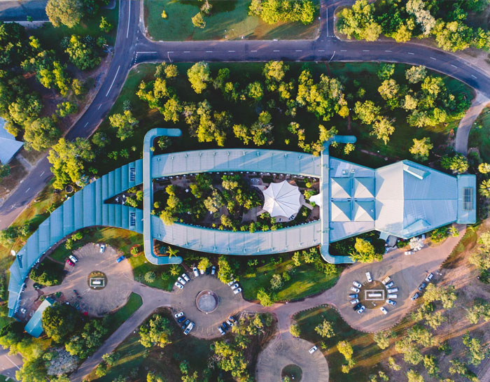 Aerial view of the bread-shaped bread factory surrounded by trees and parking areas in a green landscape.