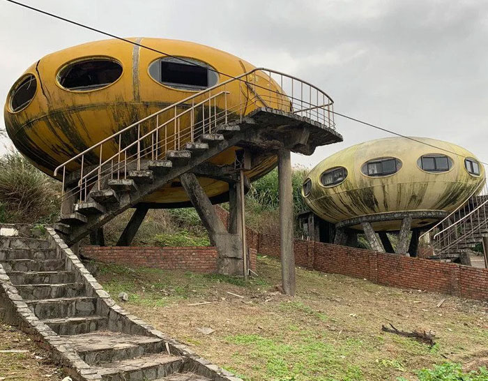 Two unusual oval-shaped buildings elevated on concrete stilts with stairs, showcasing weird architecture from around the world.