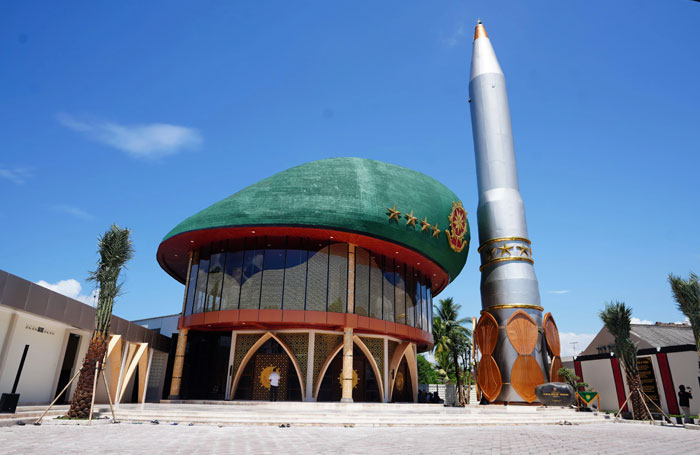 Bread-shaped bread factory building with a unique dome design and a tall rocket sculpture beside it under a clear sky.