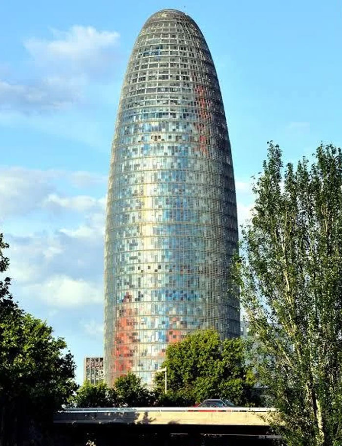 Reflective modern building shaped like a giant loaf of bread, surrounded by trees and a clear blue sky.