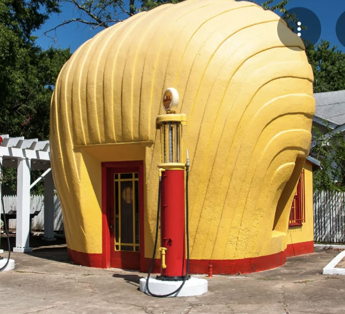Bread-shaped bread factory building in yellow with a vintage red gas pump outside on a sunny day.