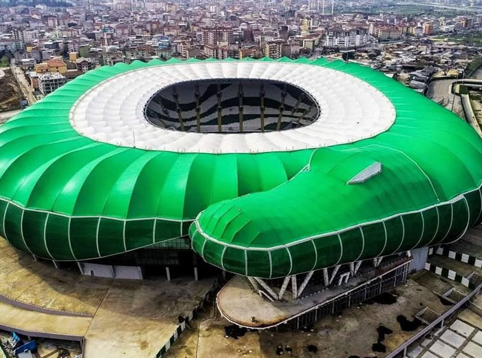 A large green stadium shaped like a snake viewed from above in an urban area featuring unique architectural design.