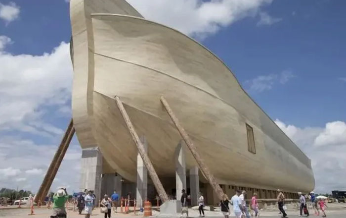 Bread-shaped bread factory building supported by beams with people walking nearby under a partly cloudy sky.