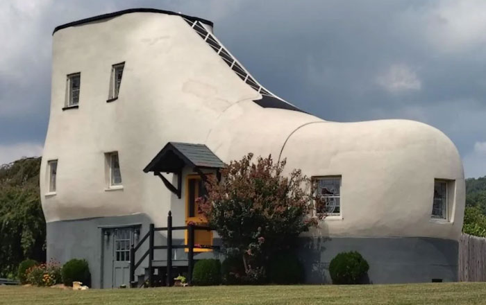 Large whimsical bread-shaped building with windows and door, resembling a giant loaf in a grassy area under cloudy sky.