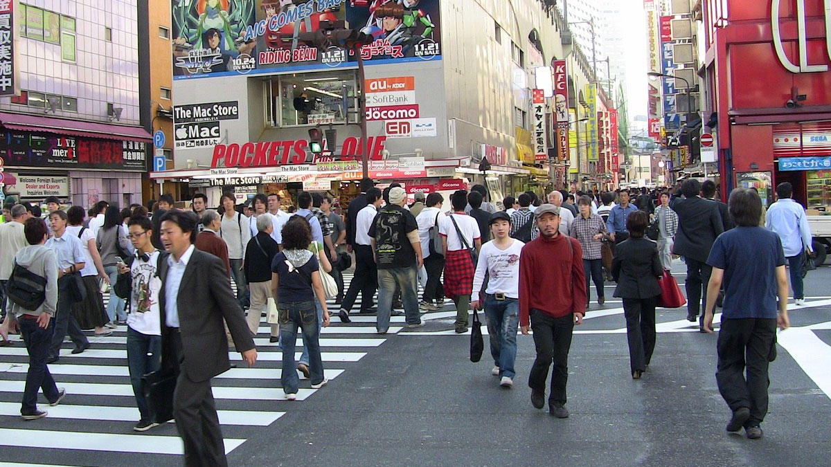 Busy city street crosswalk with pedestrians, colorful shops and signs, illustrating fascinating fun facts about urban life.