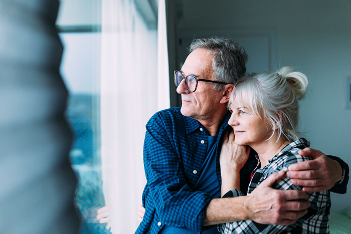 Older couple hugging and looking out window, symbolizing DNA tests revealing surprising family relationships.
