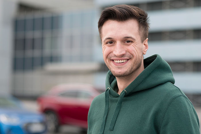 Young man smiling outdoors wearing a green hoodie, representing DNA tests revealing shocking family relationships.