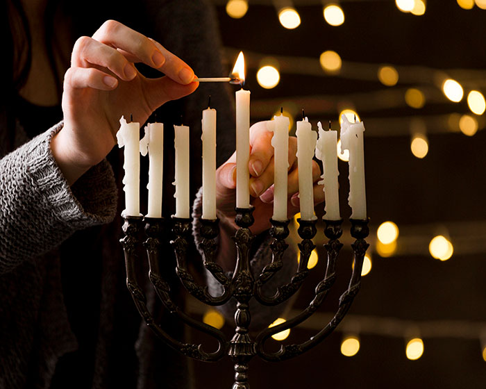 Person lighting a menorah candle with others partially melted, symbolizing family and DNA test discoveries.