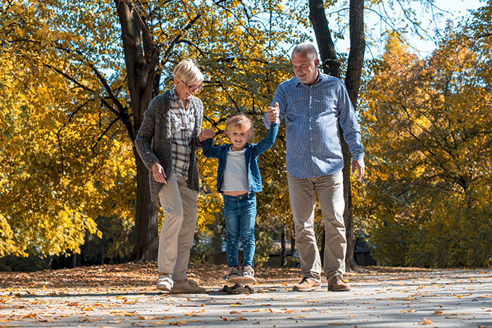 Elderly couple helping a child walk outdoors among autumn trees, representing family and DNA test discoveries.