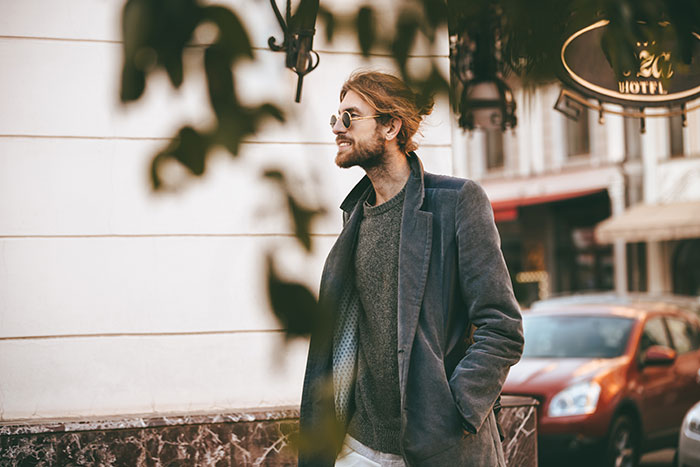 Young man wearing sunglasses and a coat standing outside with a blurred background, representing DNA tests findings.