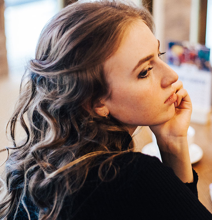 Young woman with curly hair resting her chin on her hand, reflecting on DNA test results revealing family secrets.