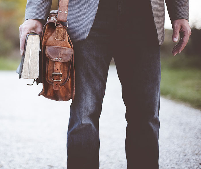Man holding a book and a leather bag walking outdoors, representing DNA tests revealing shocking family information.