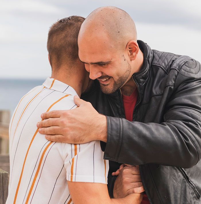 Two men hugging emotionally outdoors, illustrating surprising family DNA test results about older sister also being a mom.