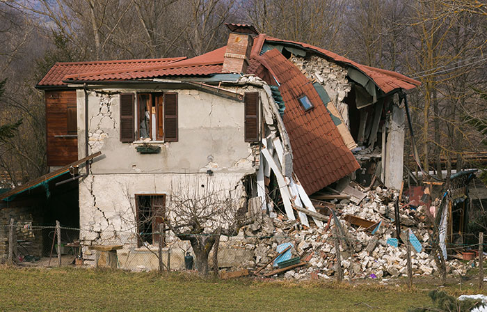 Partially collapsed house with rubble and broken roof, illustrating a strange excuse for missing work like chinchilla ate her wallet.