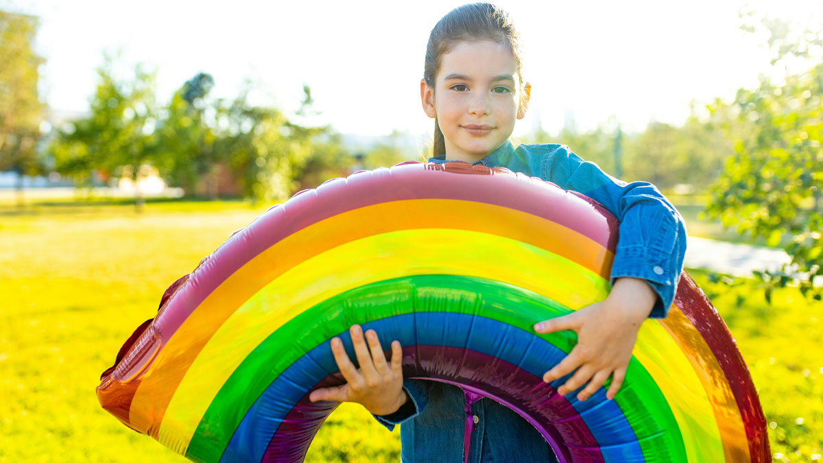 Young girl outdoors holding a large inflatable rainbow, illustrating bizarre and weird names people actually gave their children.
