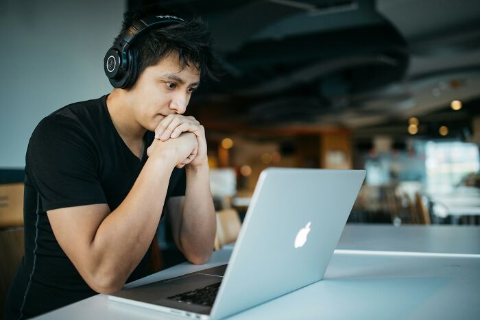 Young man wearing headphones, focused on laptop screen, representing people who became rich out of nowhere.